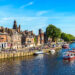 red brick buildings against blue sky, next to river with boats on